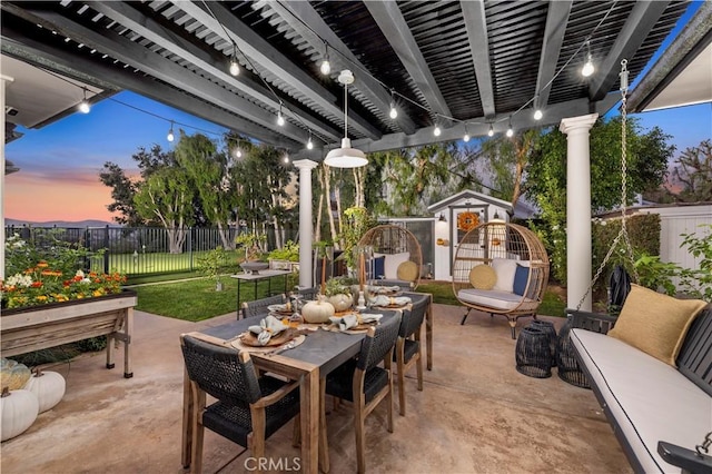 patio terrace at dusk featuring an outbuilding, a lawn, outdoor dining space, a pergola, and a fenced backyard