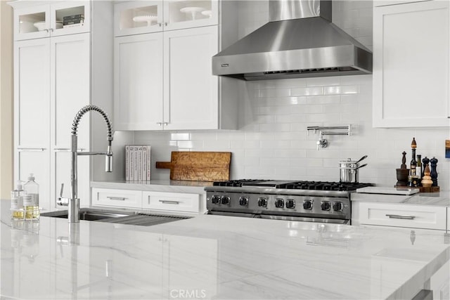 kitchen with a sink, light stone counters, backsplash, wall chimney exhaust hood, and stove