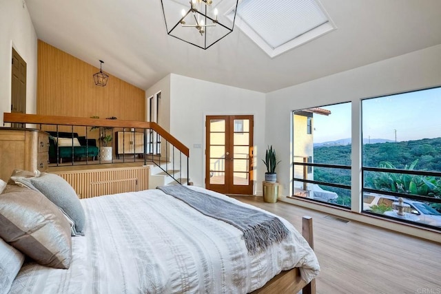 bedroom featuring vaulted ceiling, a notable chandelier, wood walls, light wood-type flooring, and french doors