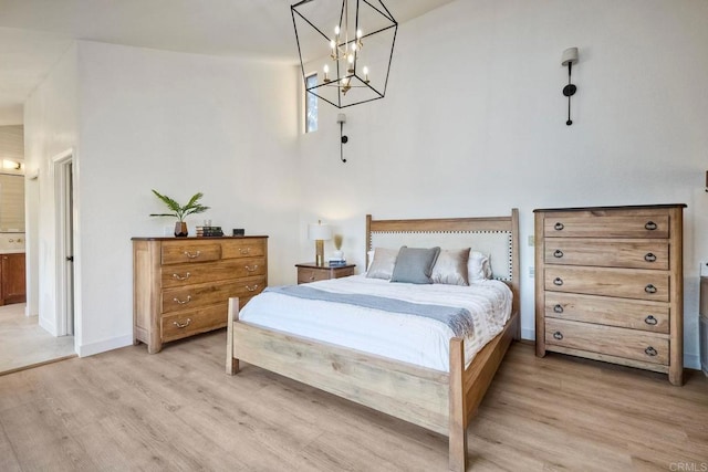 bedroom with connected bathroom, a notable chandelier, and light wood-type flooring