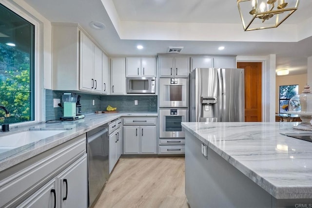 kitchen featuring an inviting chandelier, stainless steel appliances, decorative backsplash, decorative light fixtures, and light wood-type flooring