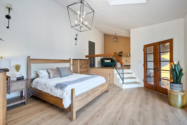 bedroom featuring wood walls, a chandelier, light hardwood / wood-style floors, and french doors