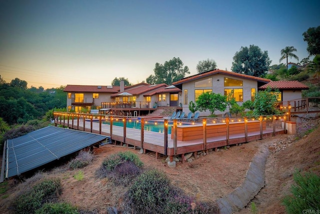 back house at dusk featuring a pool side deck