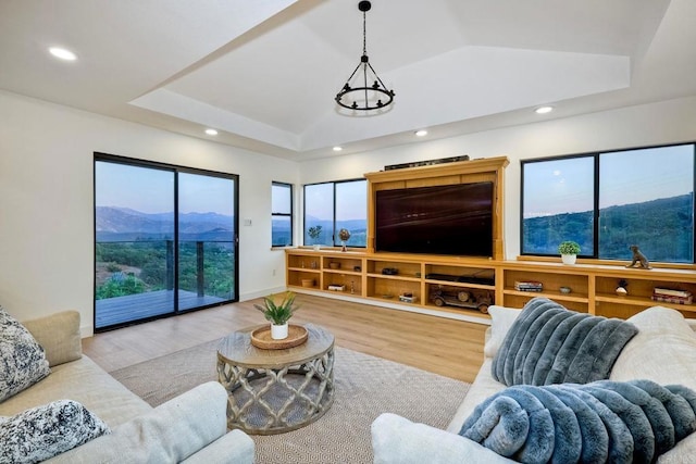 living room featuring lofted ceiling, built in features, a raised ceiling, and light wood-type flooring