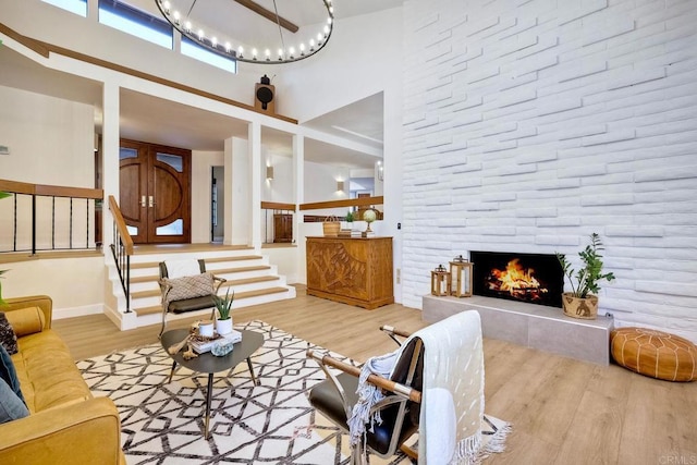 living room featuring light wood-type flooring, an inviting chandelier, a fireplace, and a high ceiling