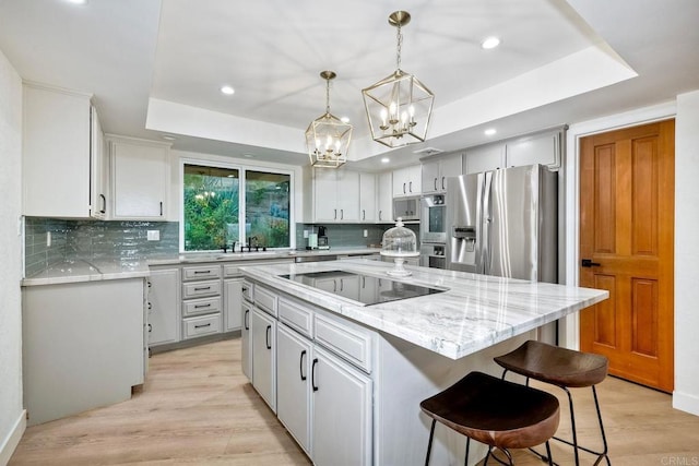 kitchen featuring stainless steel fridge with ice dispenser, black electric stovetop, a kitchen island, and a tray ceiling