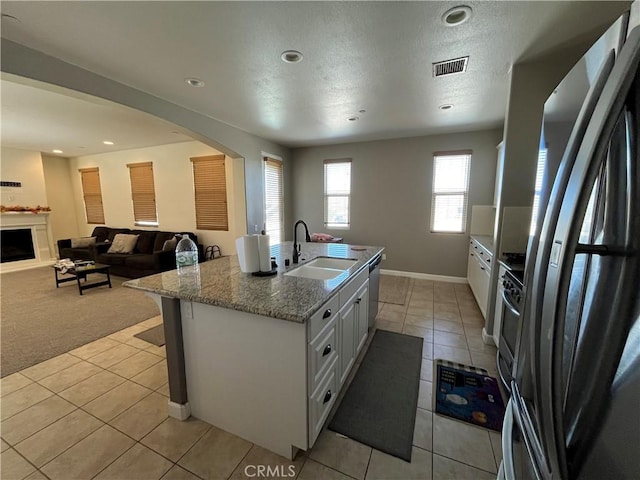 kitchen with appliances with stainless steel finishes, light colored carpet, a kitchen island with sink, sink, and white cabinetry