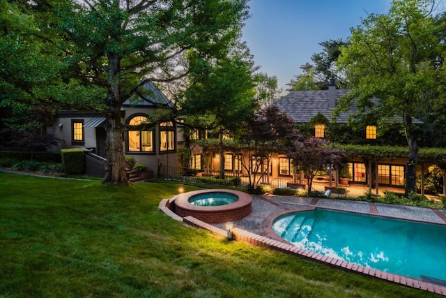 pool at dusk featuring a yard and an in ground hot tub