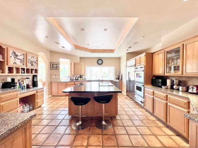 kitchen featuring a breakfast bar, a tray ceiling, a kitchen island, light brown cabinets, and double oven