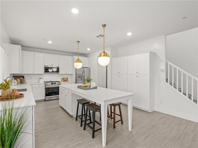 kitchen with appliances with stainless steel finishes, sink, pendant lighting, a center island, and white cabinetry