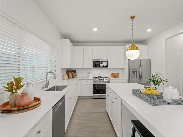 kitchen featuring white cabinetry, sink, decorative light fixtures, appliances with stainless steel finishes, and light wood-type flooring