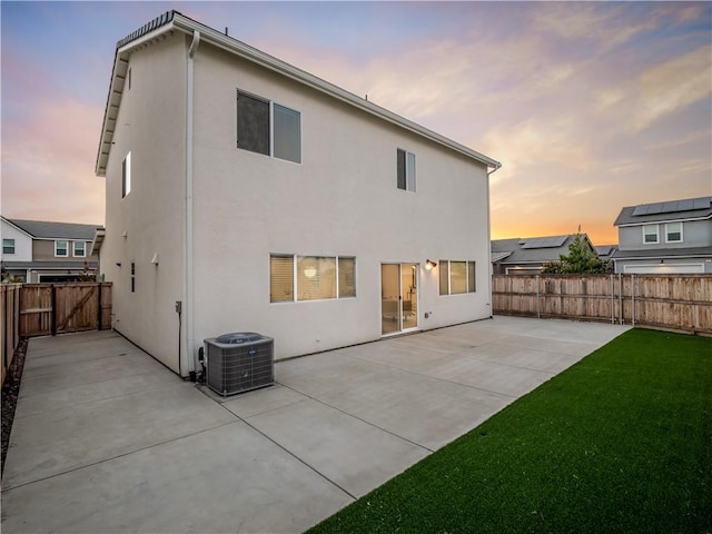 back house at dusk with cooling unit, a patio area, and a yard