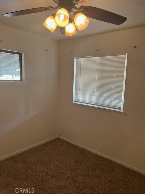 empty room featuring ceiling fan and dark colored carpet