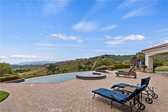 view of patio featuring a mountain view, an in ground hot tub, and a playground