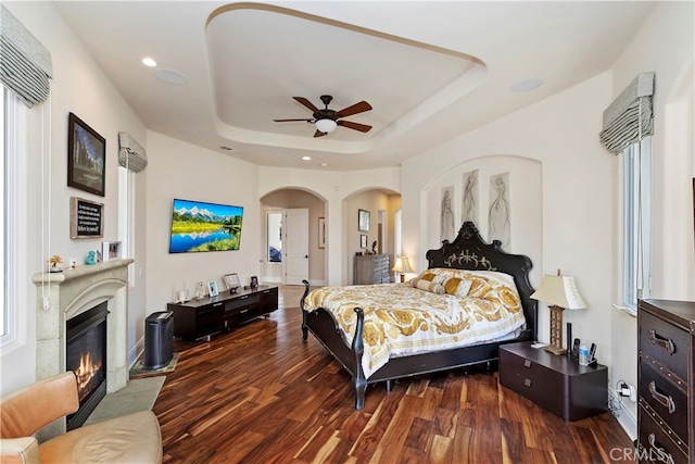 bedroom with dark hardwood / wood-style flooring, multiple windows, ceiling fan, and a raised ceiling