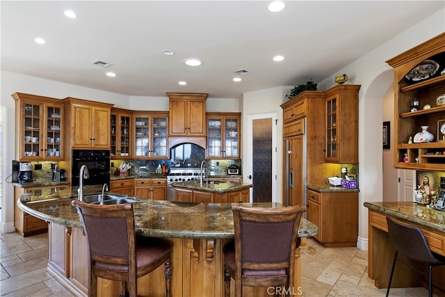 kitchen featuring decorative backsplash, dark stone counters, and an island with sink