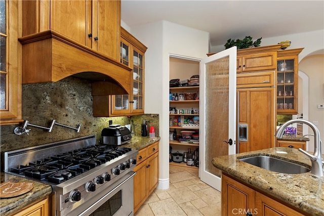 kitchen featuring stainless steel range, sink, light tile patterned floors, decorative backsplash, and light stone countertops