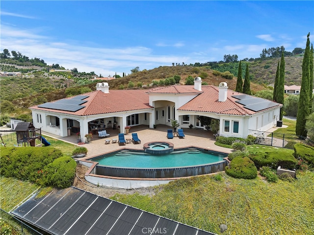 back of house featuring solar panels, a patio area, and a swimming pool with hot tub