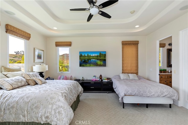 carpeted bedroom with a tray ceiling, ensuite bath, and ceiling fan