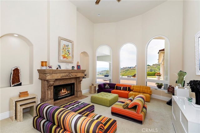 living room featuring ceiling fan, carpet flooring, a premium fireplace, and a high ceiling