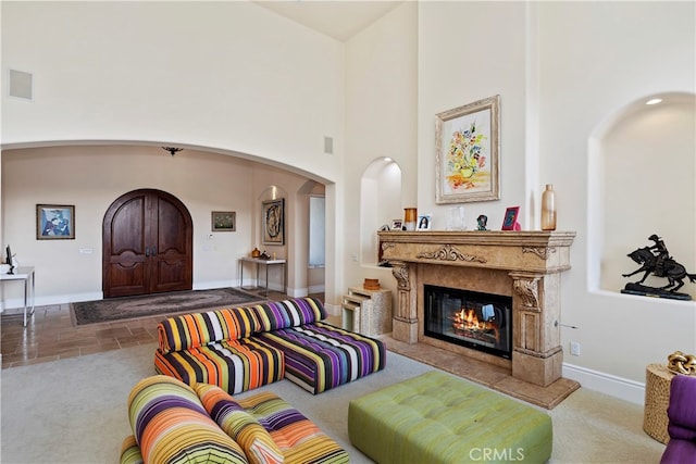 carpeted living room with a high end fireplace and a high ceiling