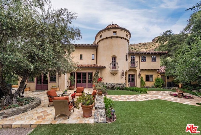 back of house featuring outdoor lounge area, a patio area, a balcony, and a lawn