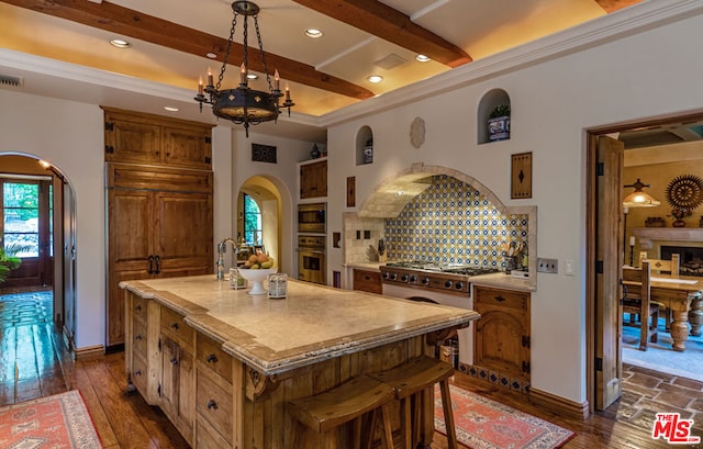 kitchen with beamed ceiling, dark hardwood / wood-style flooring, stainless steel appliances, and a kitchen island with sink