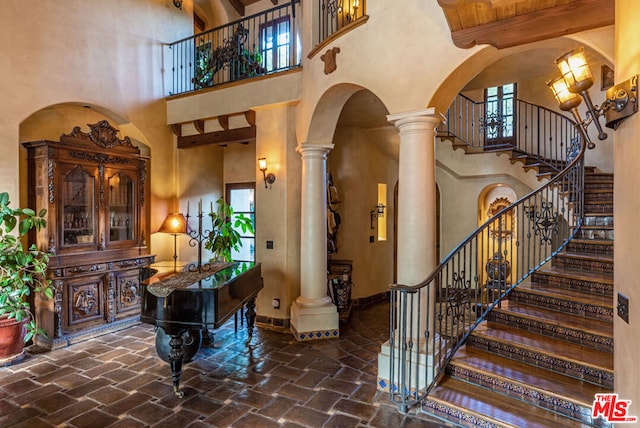 entryway featuring beam ceiling, ornate columns, and a high ceiling