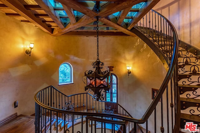 stairs with beamed ceiling, a high ceiling, and hardwood / wood-style flooring