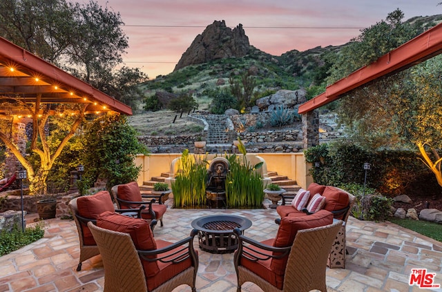 patio terrace at dusk featuring a mountain view and an outdoor living space with a fire pit