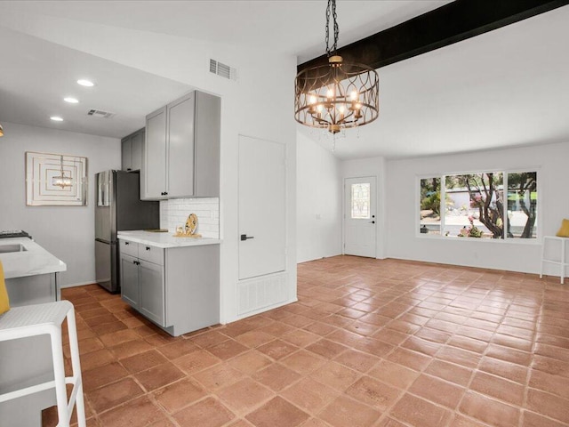 kitchen with stainless steel fridge, gray cabinetry, decorative backsplash, and an inviting chandelier