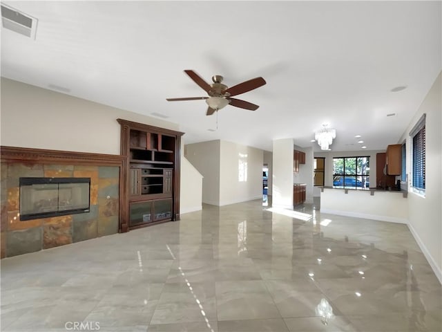 unfurnished living room featuring ceiling fan with notable chandelier and a tiled fireplace