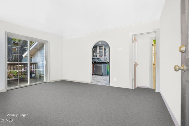 unfurnished room with baseboards, arched walkways, and carpet floors