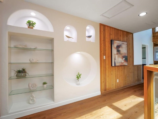 corridor with built in shelves, light wood-type flooring, and wood walls