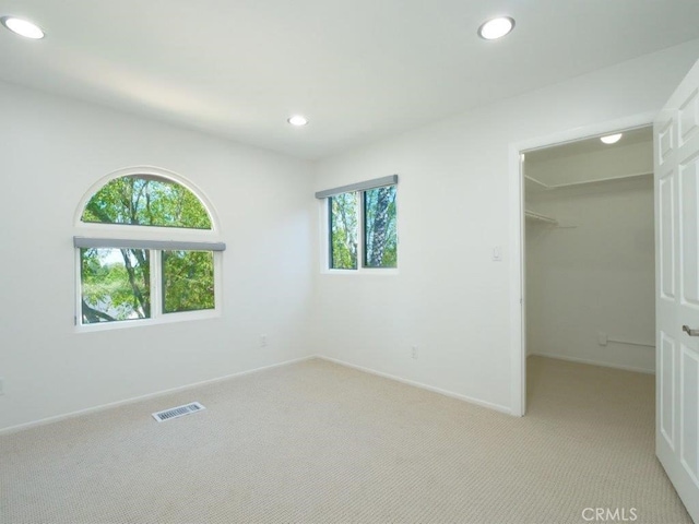 unfurnished bedroom with light colored carpet, a closet, and a spacious closet