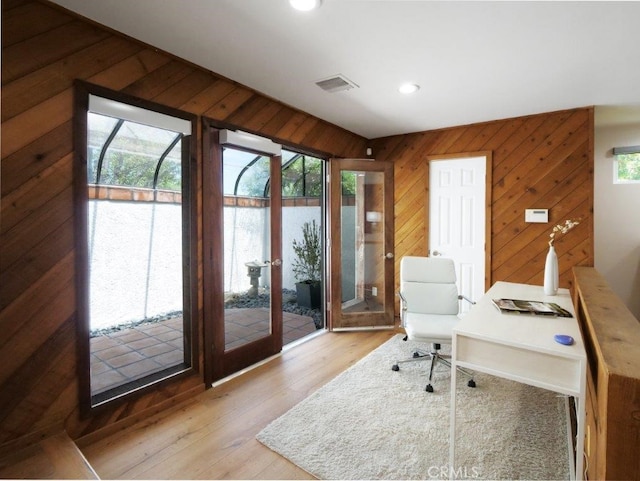 home office with wood walls and light hardwood / wood-style flooring