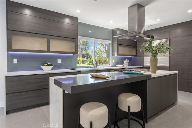 kitchen featuring tasteful backsplash, a center island, sink, island exhaust hood, and a kitchen breakfast bar