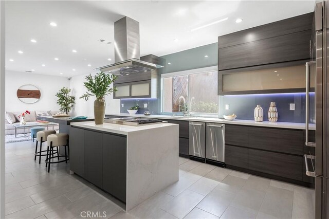 kitchen with appliances with stainless steel finishes, a kitchen island, sink, island range hood, and a breakfast bar