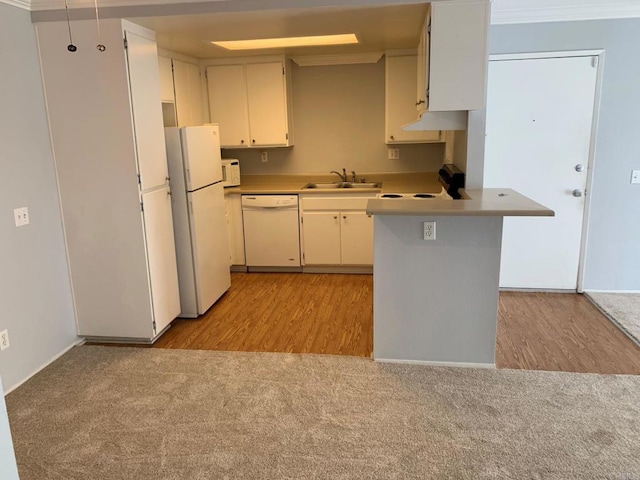 kitchen featuring crown molding, wall chimney exhaust hood, white appliances, light colored carpet, and kitchen peninsula