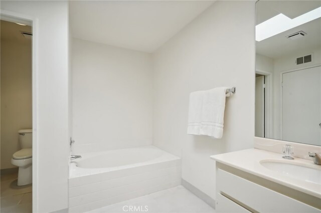 bathroom with vanity, toilet, tiled bath, and tile patterned flooring