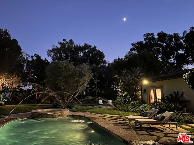 pool at dusk with an in ground hot tub and a patio area