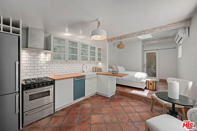 kitchen featuring white cabinets, wall chimney range hood, a barn door, butcher block counters, and stainless steel appliances