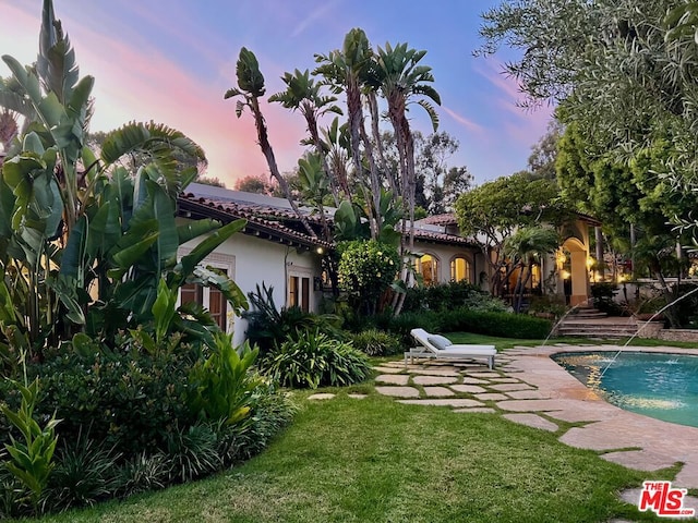 back house at dusk with pool water feature, a patio area, and a lawn