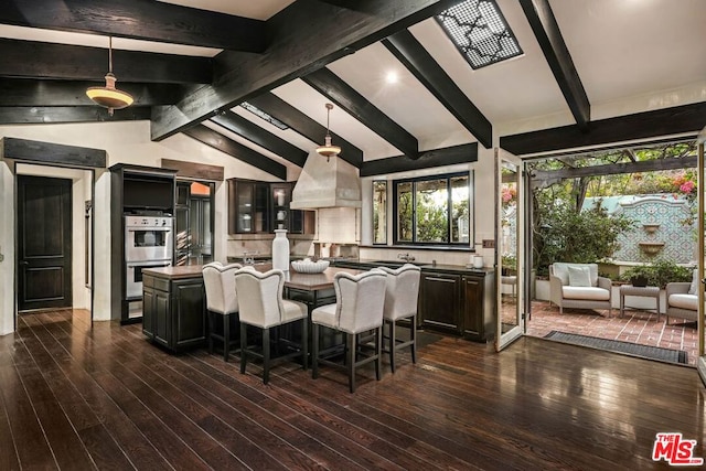 kitchen with vaulted ceiling with beams, a kitchen island, hanging light fixtures, and dark wood-type flooring