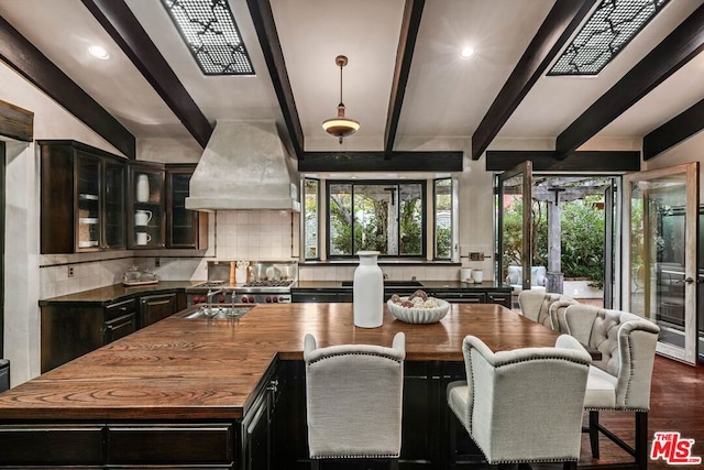 kitchen featuring tasteful backsplash, custom exhaust hood, dark wood-type flooring, beamed ceiling, and a kitchen island