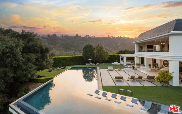 pool at dusk with a patio and a yard