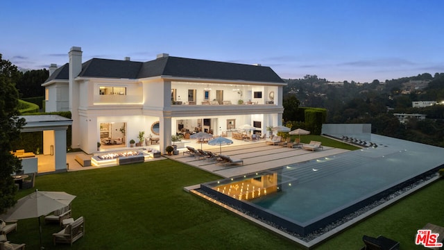 back house at dusk with an outdoor fire pit, a patio, and a lawn