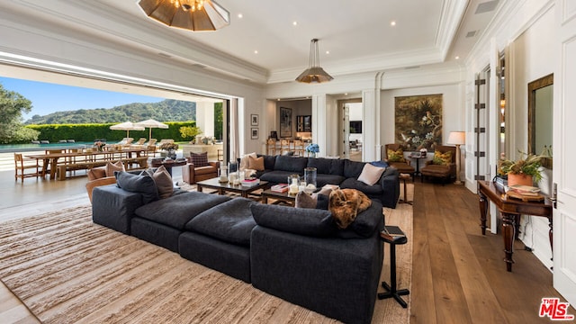 living room featuring ceiling fan, a tray ceiling, light hardwood / wood-style flooring, ornamental molding, and a mountain view