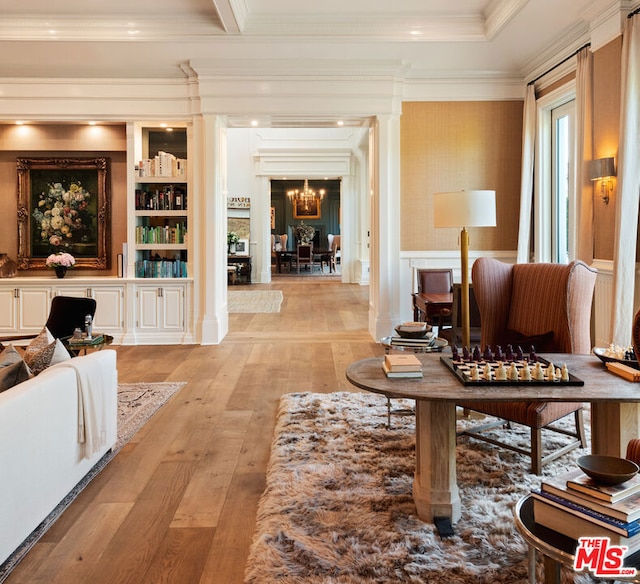 interior space featuring ornate columns, crown molding, a notable chandelier, built in shelves, and light hardwood / wood-style floors