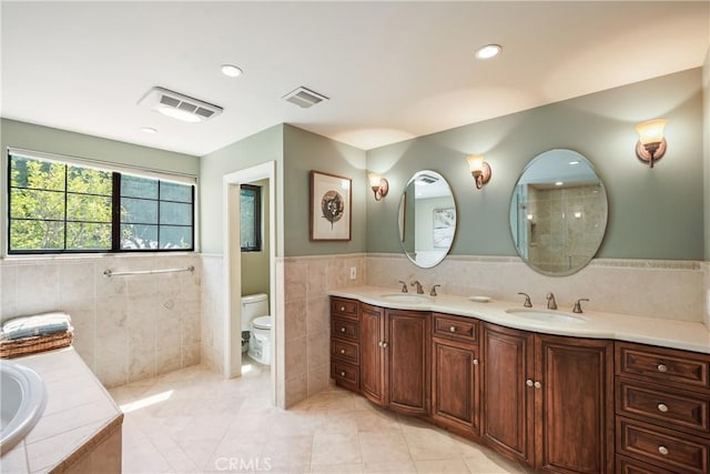 bathroom featuring vanity, tile walls, tile patterned flooring, tiled bath, and toilet